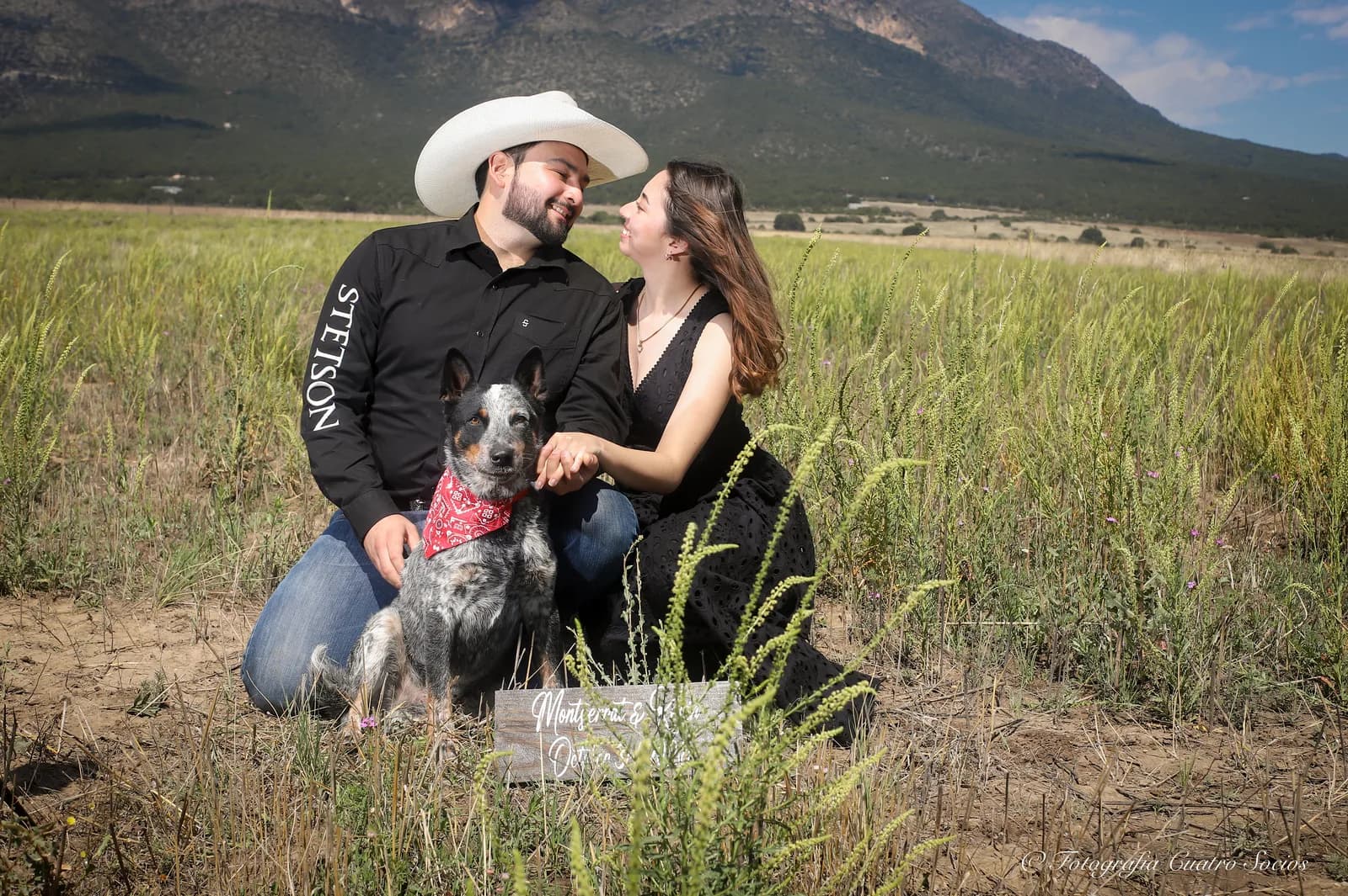 Una pareja sentada con su perro frente a las montañas